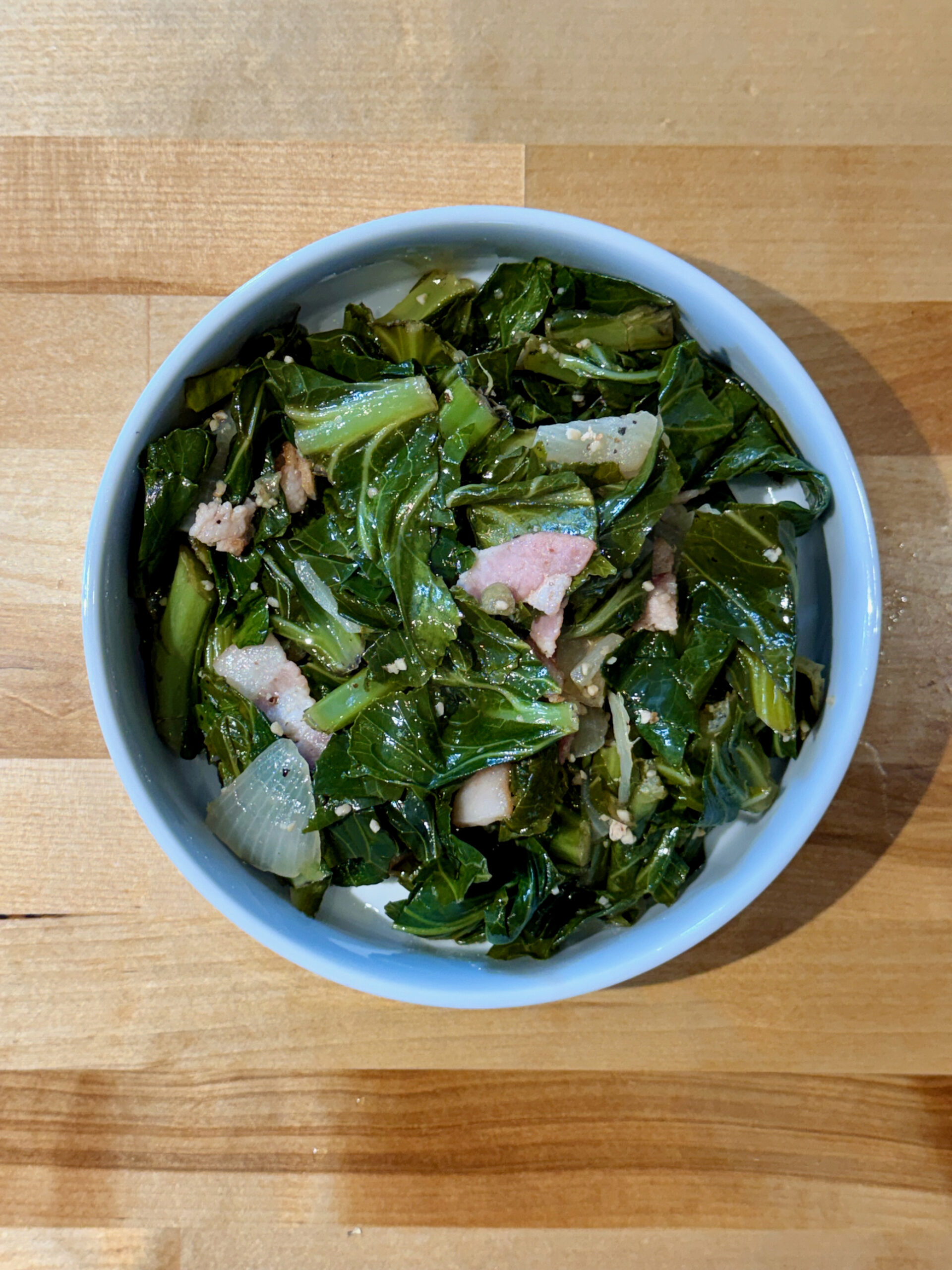 Cooked collard greens with bacon and onions in a white bowl