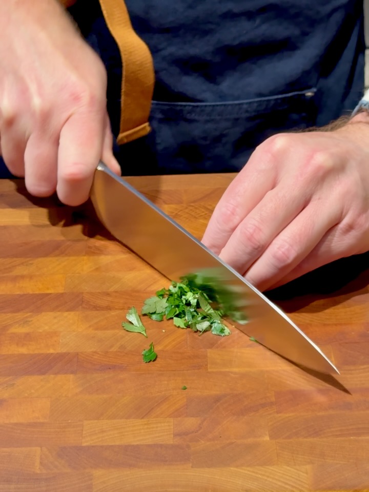 Ross chopping Italian parsley with a chef's knife on a wooden cutting board