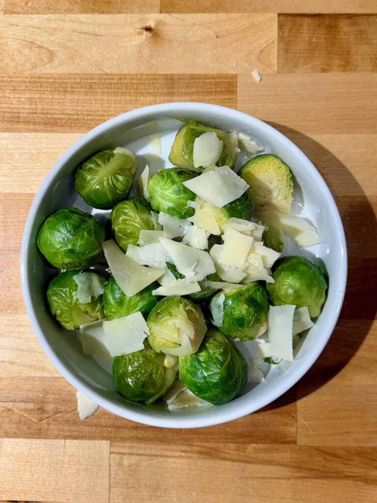 White bowl with cooked Brussels sprouts topped with shaved parmesan cheese