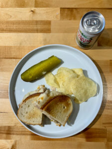 White plate with finished tuna melt, potato chips and pickle on the side with a small can of zero sugar Canada Dry ginger ale