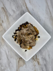 White square bowl with cooked rice, black beans, and pulled pork inside