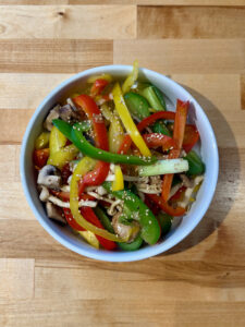 White bowl with finished stir fry of green, red and yellow bell peppers, mushrooms and a sprinkling of white sesame seeds
