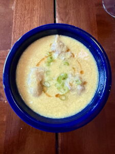Blue bowl with egg drop soup with wontons a swirl of sesame oil and chopped scallions