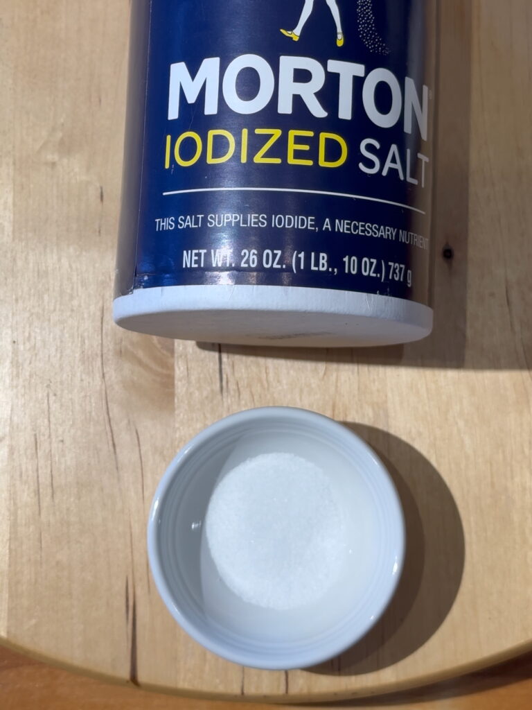 Canister of Mortons iodized table salt with a small white dish containing table salt