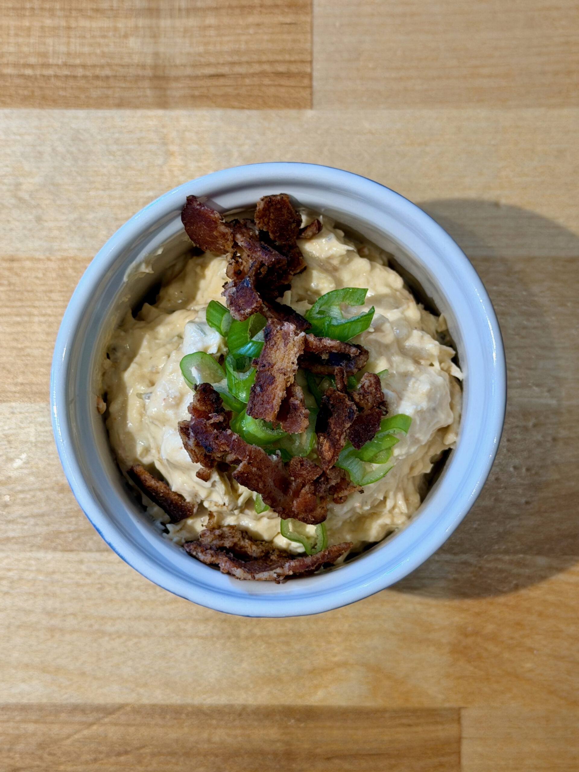 Ramekin with cheesy chicken dip topped with crispy bacon bits and sliced green onions