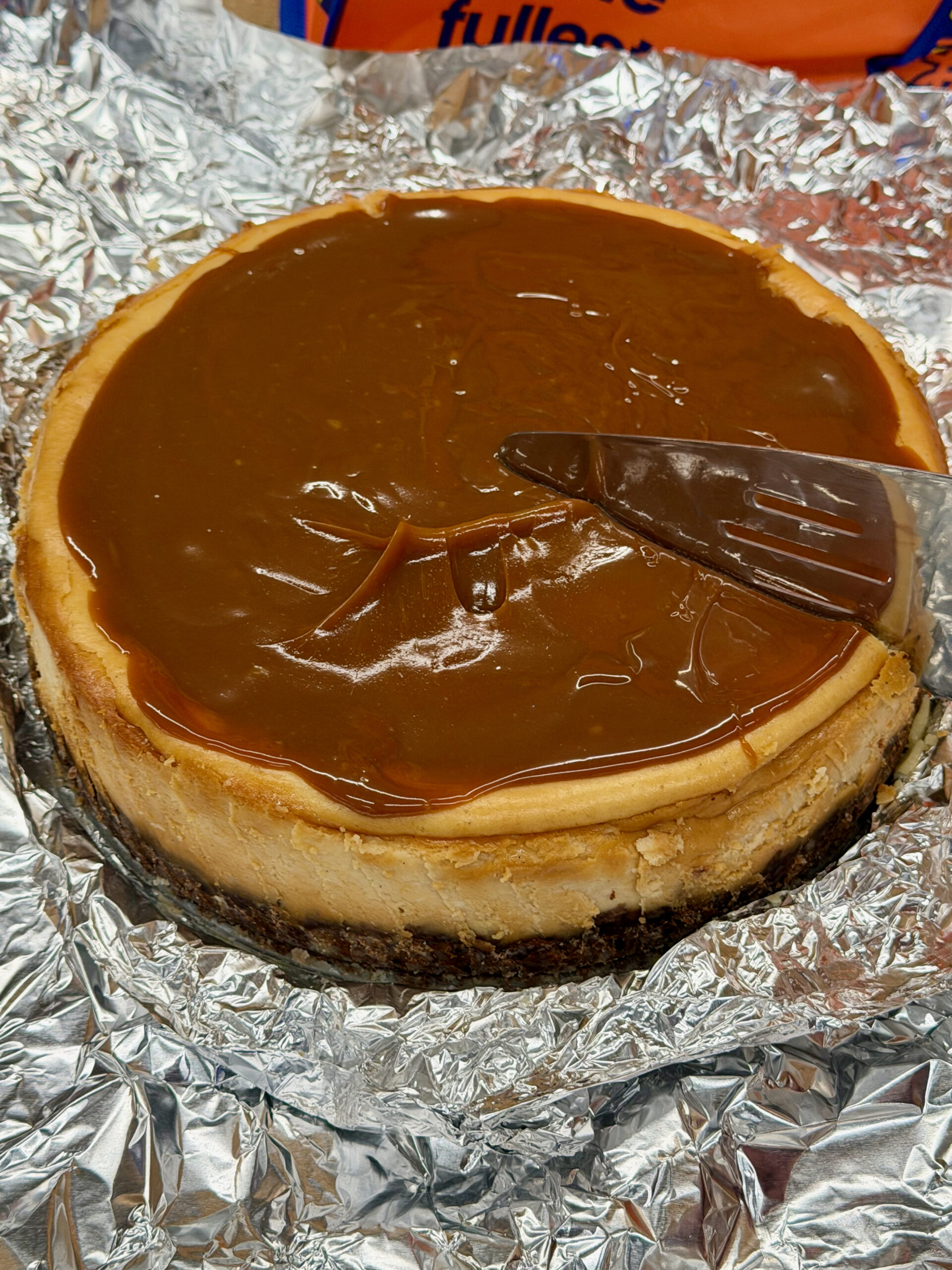 Dulce de leche full cake on aluminum foil with a cake server getting ready to cut the cheesecake
