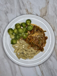 Finished chicken and sauce with grated parmesan cheese and steamed Brussels Sprouts with herb pasta as sides on a white plate