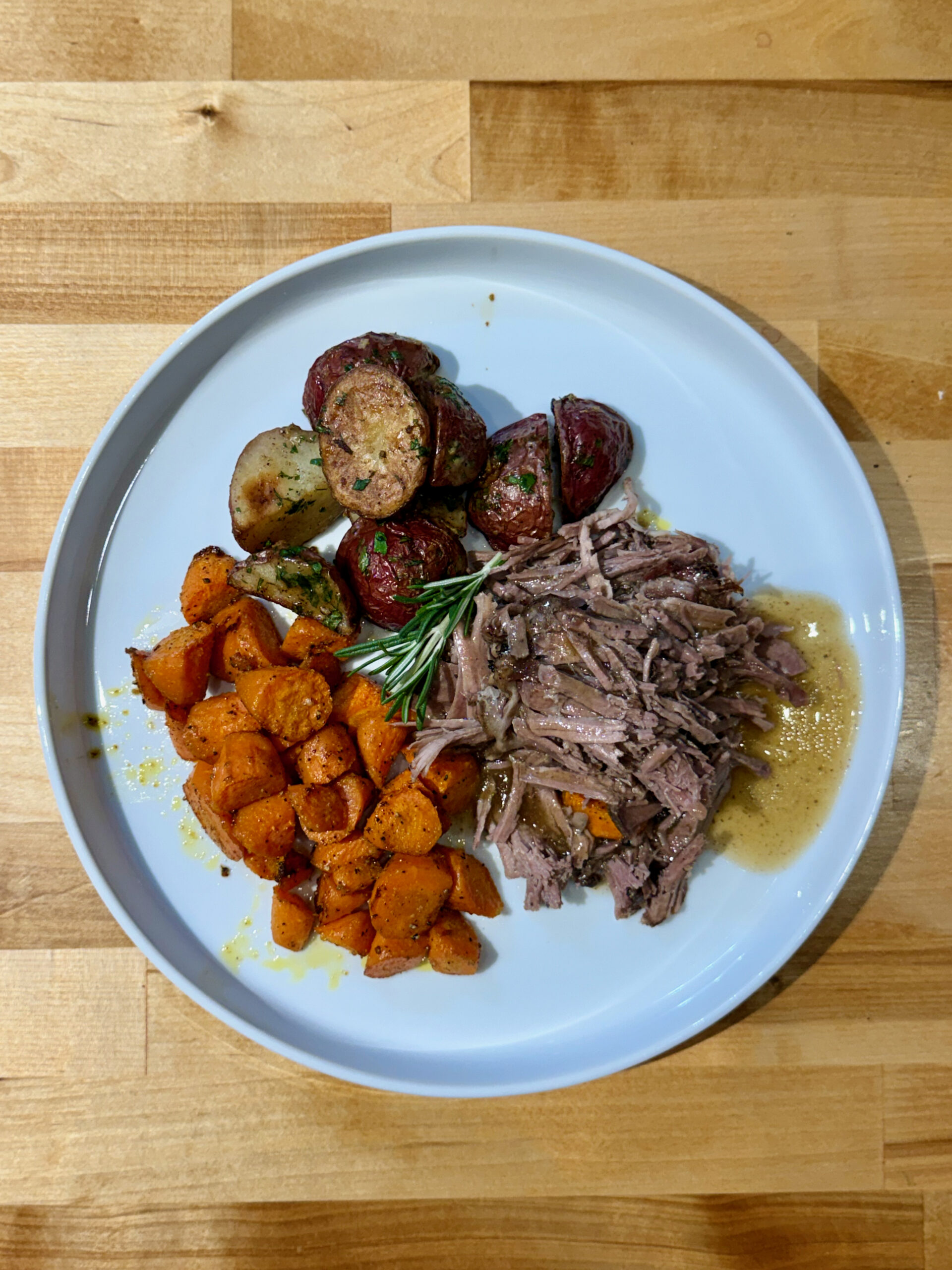 White plate with shredded slow cooked leg of lamb, oblique cut roasted carrots and roasted parsley red potatoes