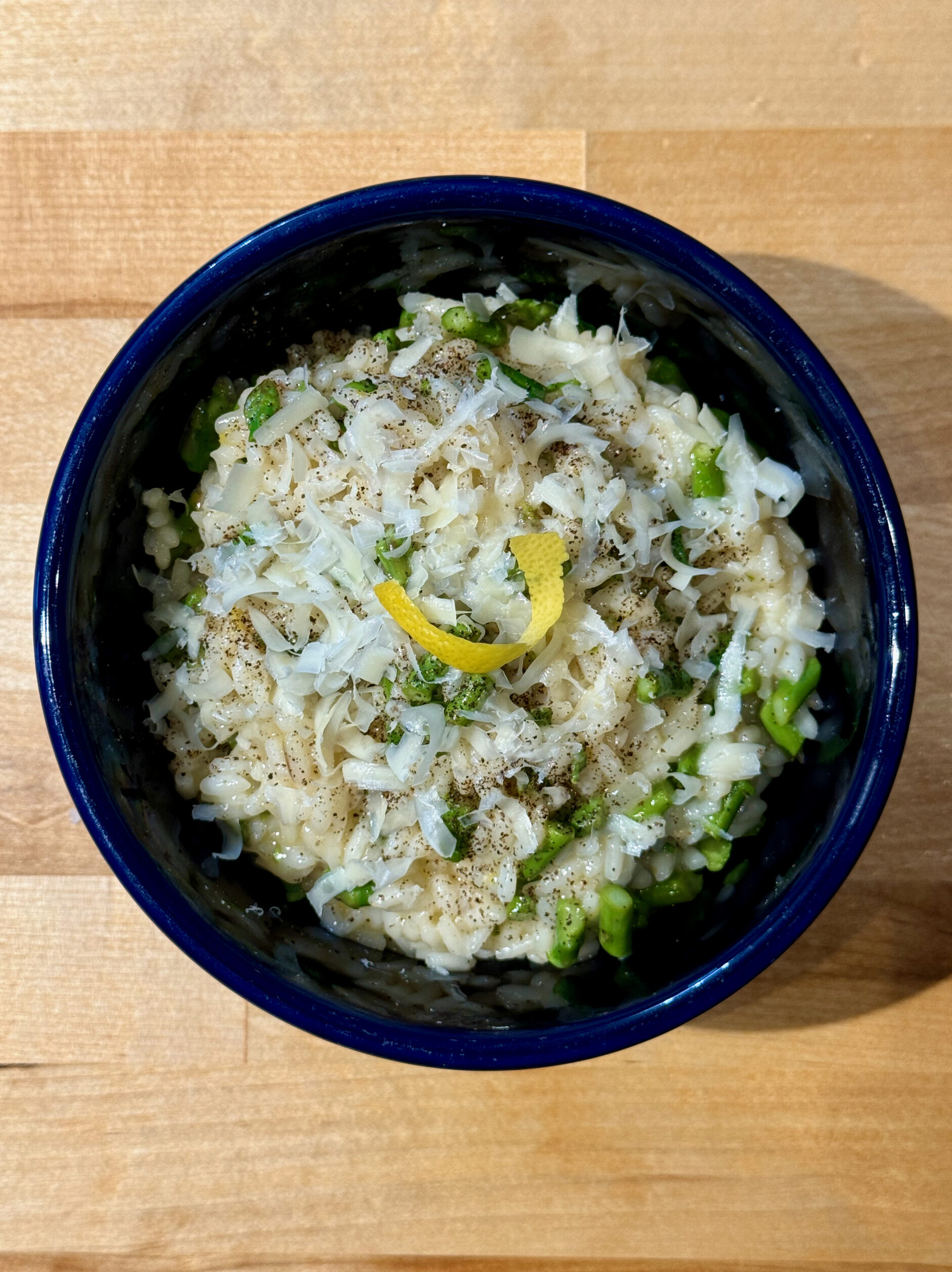 Creamy lemon asparagus risotto in a blue bowl with shaved parmesan and a twist of lemon on top