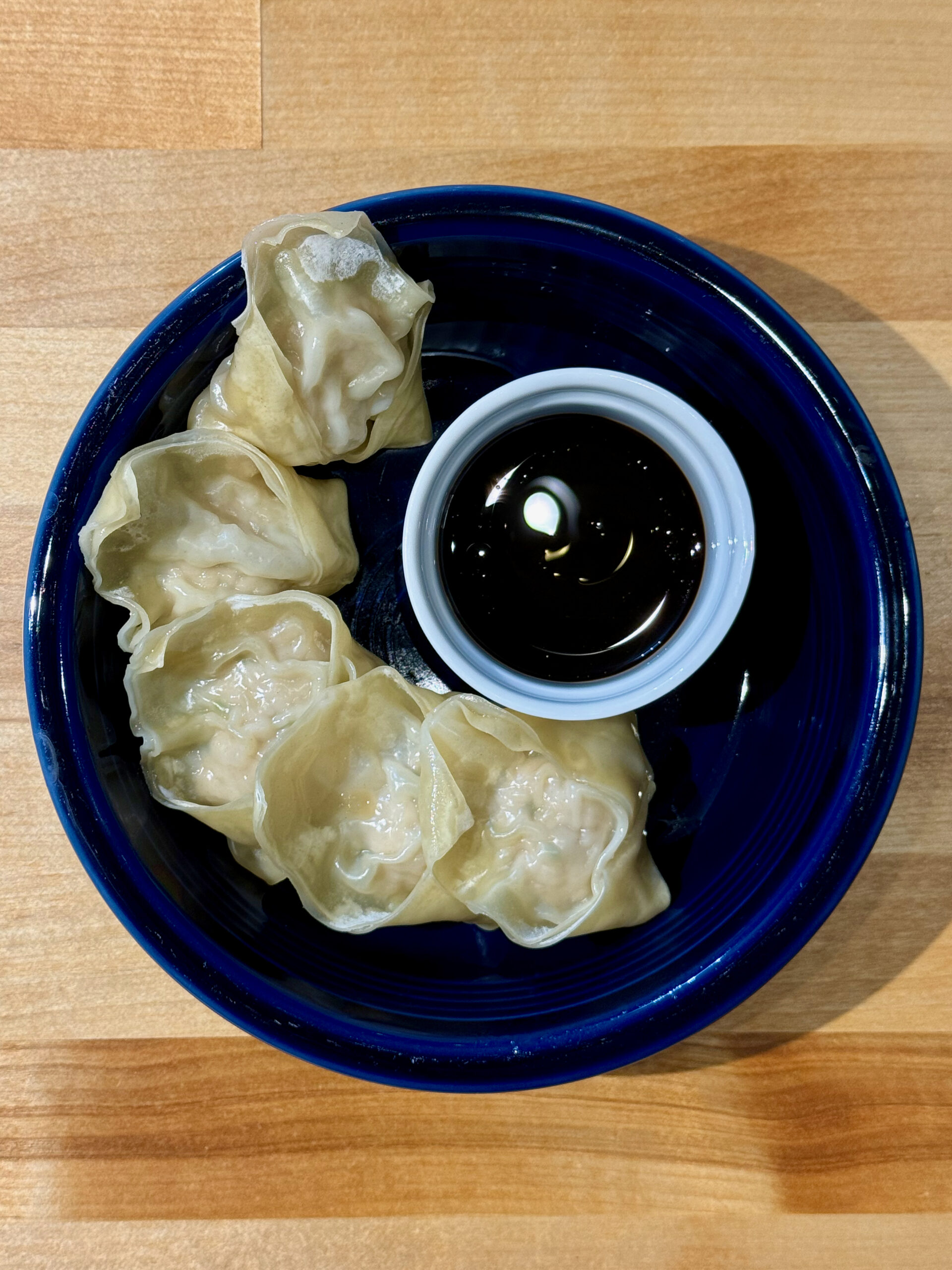 Blue bowl with five steamed pork wontons and a small ramekin of dipping sauce