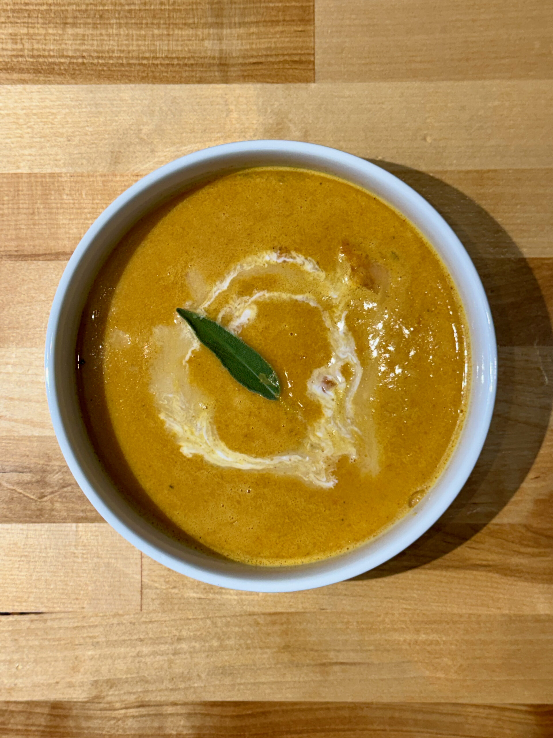 White soup bowl with cooked spicy gochujang carrot soup with a swirl of coconut milk and sage leaf.