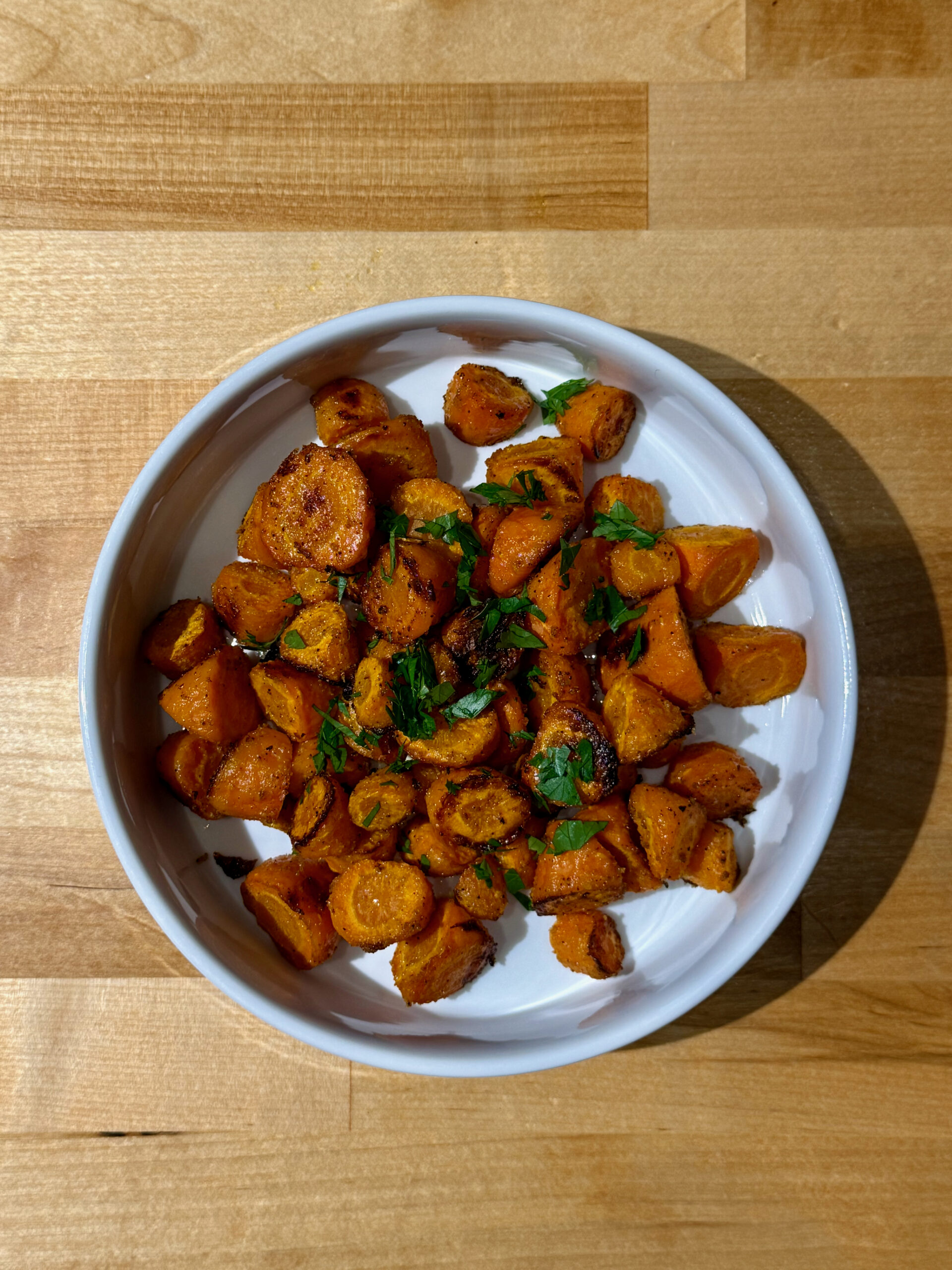 Roasted Carrots in a white bowl with fresh parsley sprinkled on top