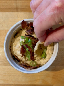 Hand with scoop corn chip taking a scoop of buffalo chicken dip