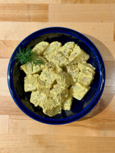 Finished mustard potato salad in a blue bowl with freshly ground black pepper and a sprig of dill on top