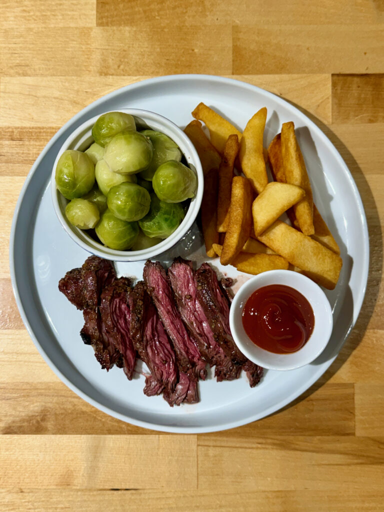 Grilled Skit Steak, Steamed Brussels Sprouts, Cooked Steak Fries and ketchup on a white plate