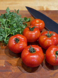 Tomatoes and fresh cilantro with a chef's knife on a bamboo cutting board