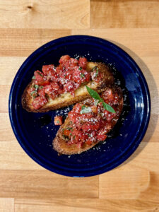 Two pieces of Balsamic Bruschetta on a blue salad plate with fresh grated parmesan cheese and basil on top