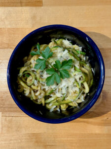 Fresh zoodles in a blue bowl topped with parmesan cheese and parsley