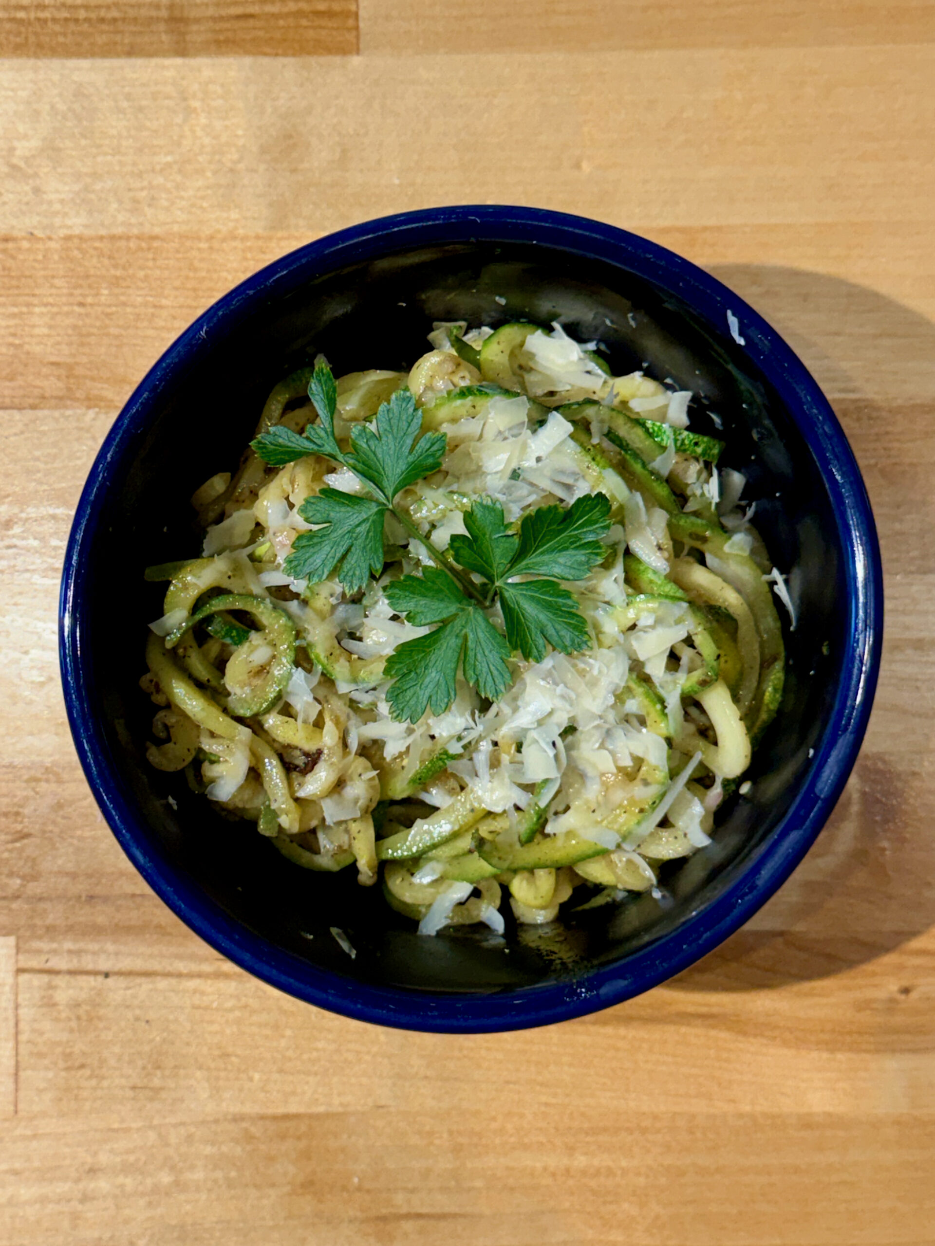 Fresh zoodles in a blue bowl topped with parmesan cheese and parsley