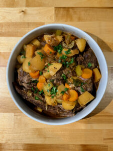 Finished pot roast and vegetables in a large white serving dish with parsley sprinkled on top
